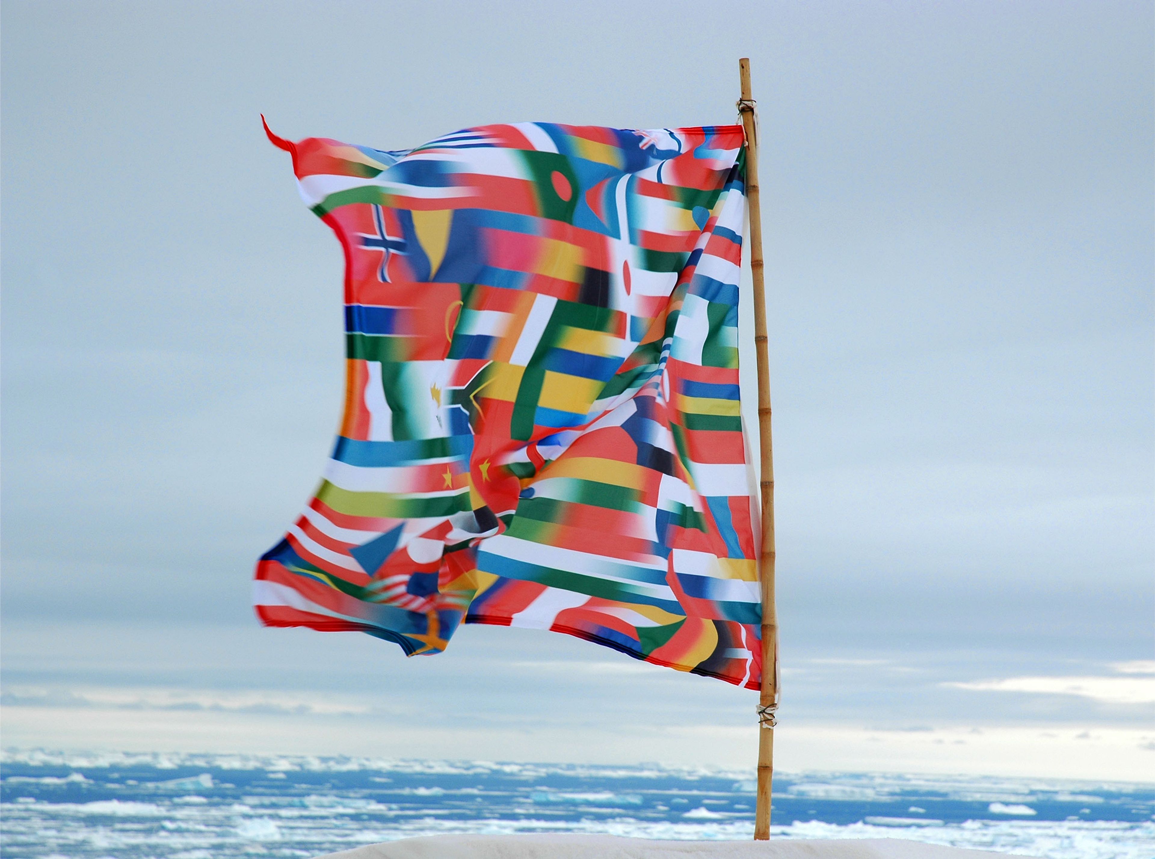 Image shows a flag in the Antarctic landscape made up of different flags. 