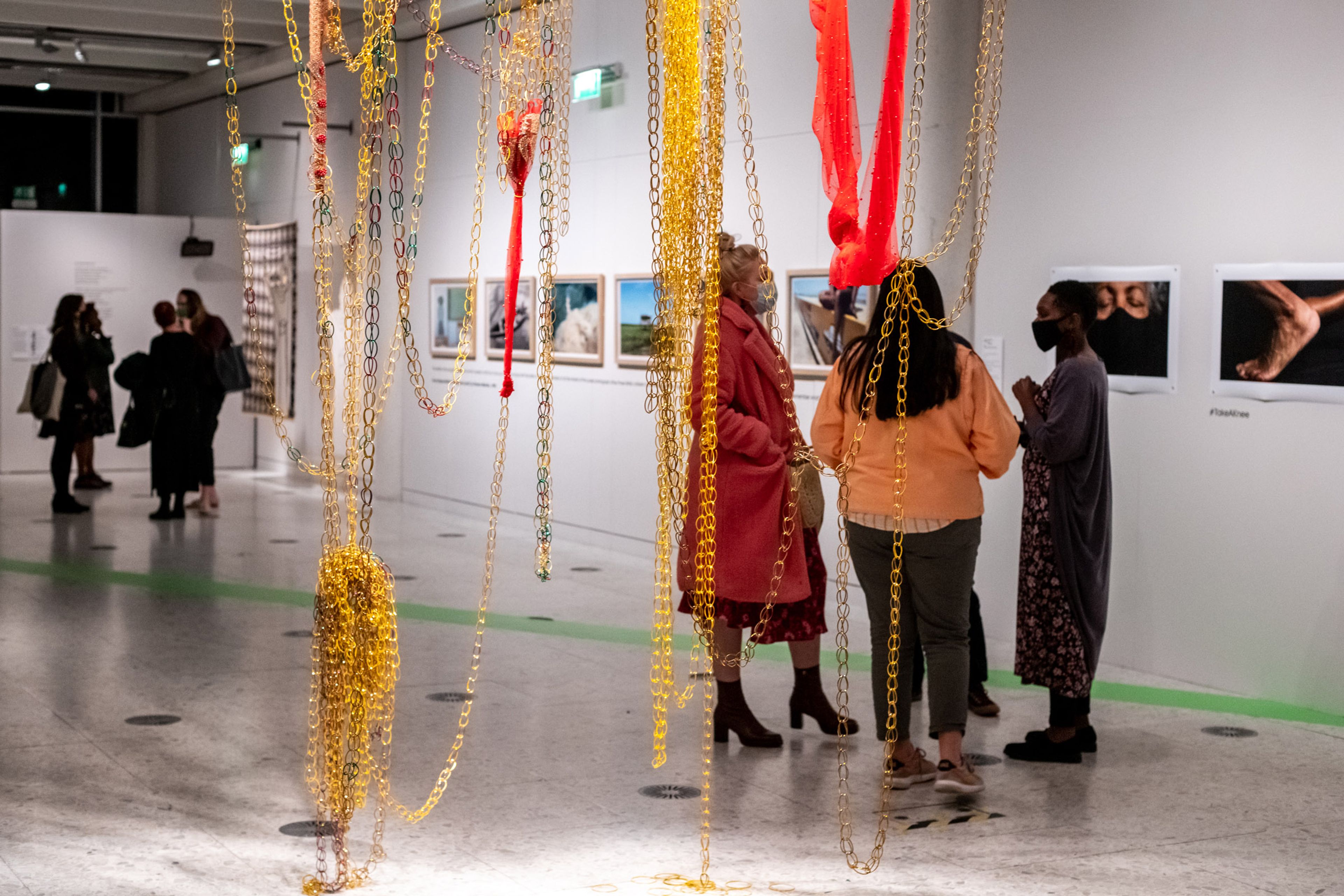 A large installation of fabric and chains hangs from a gallery ceiling in front of spectators.