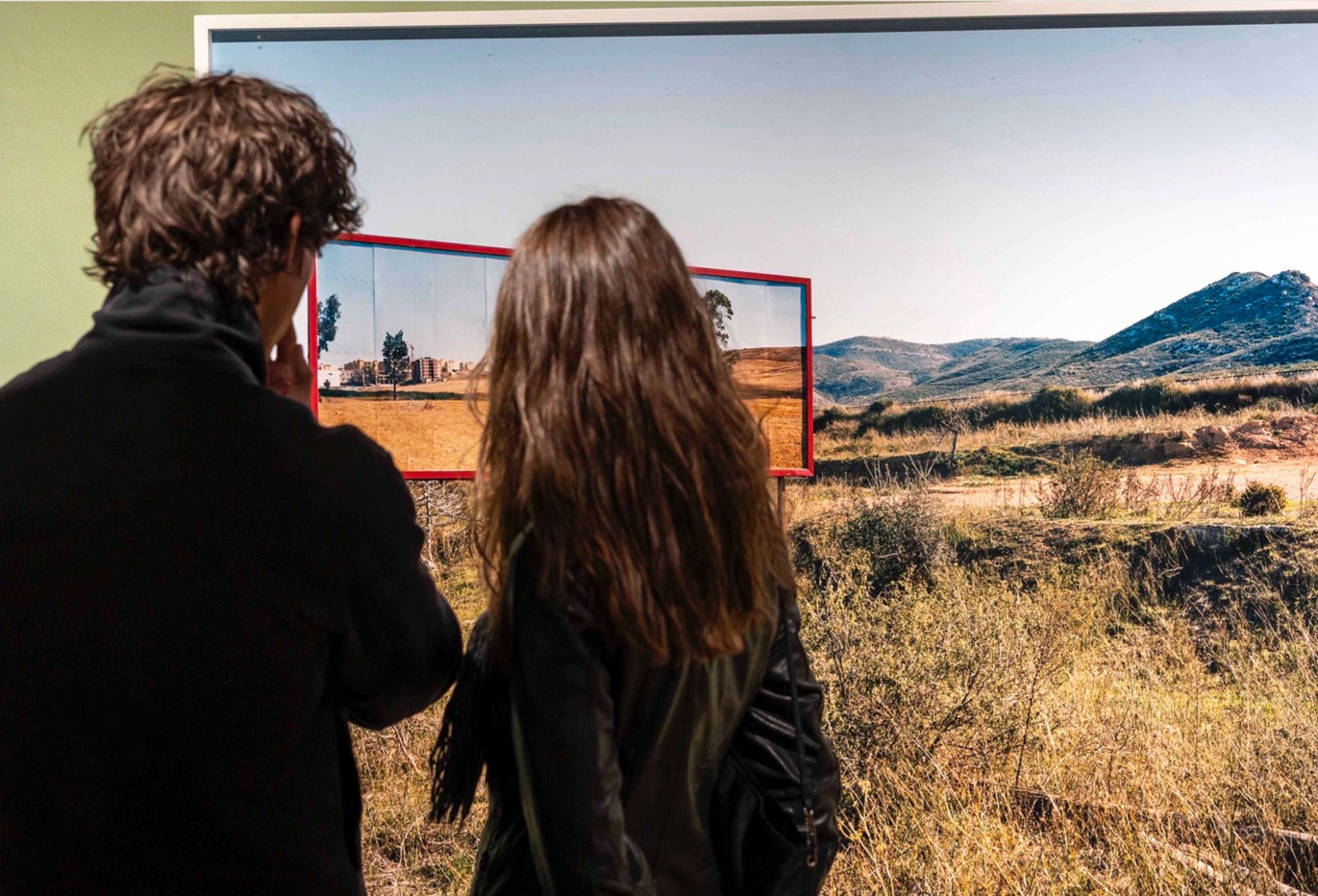 Two visitors view Corinne Silva’s landscape artwork in the BorderLands exhibition.