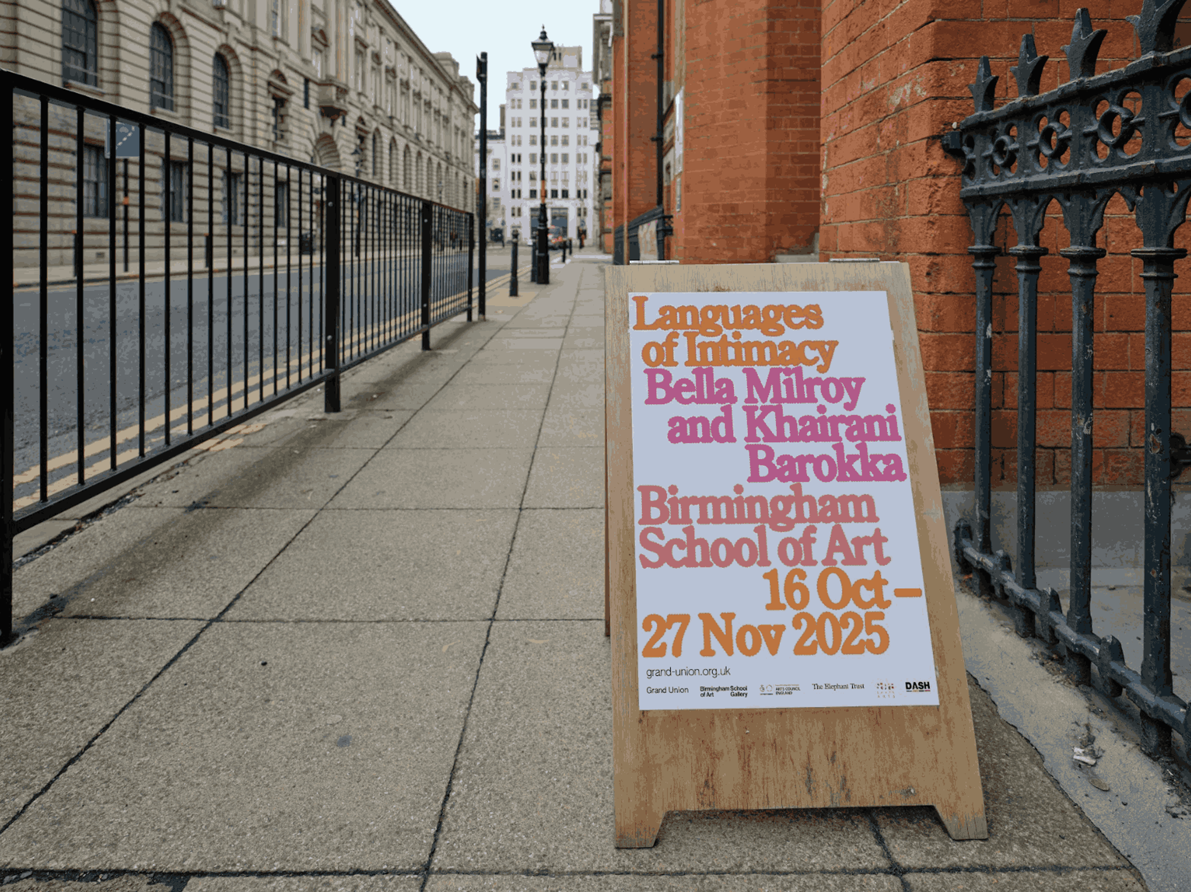 A poster board on a street with orange and pink text reading 'Languages of Intimacy'.