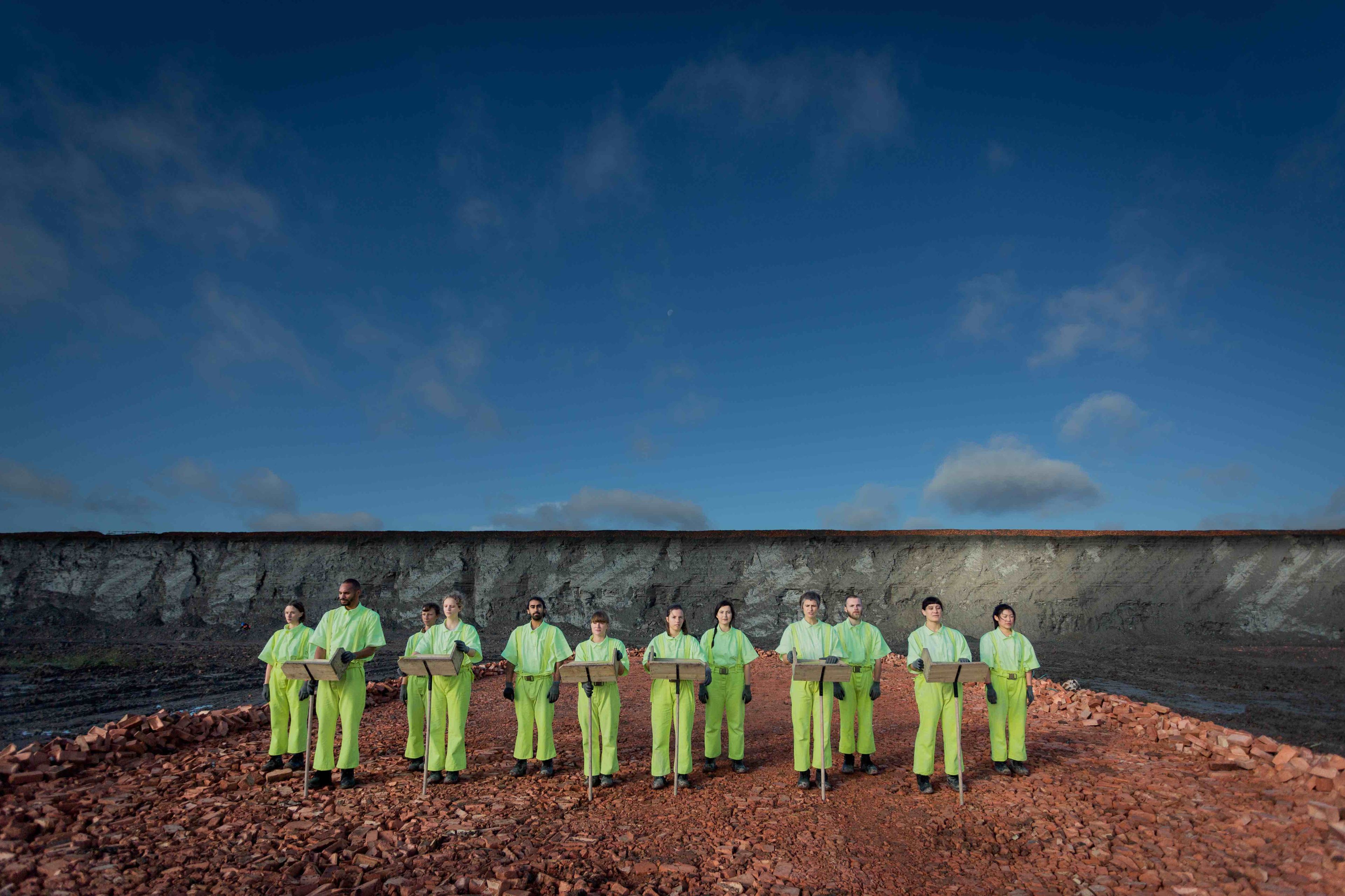 A group of performers dressed in lime green, stood in a quarry.