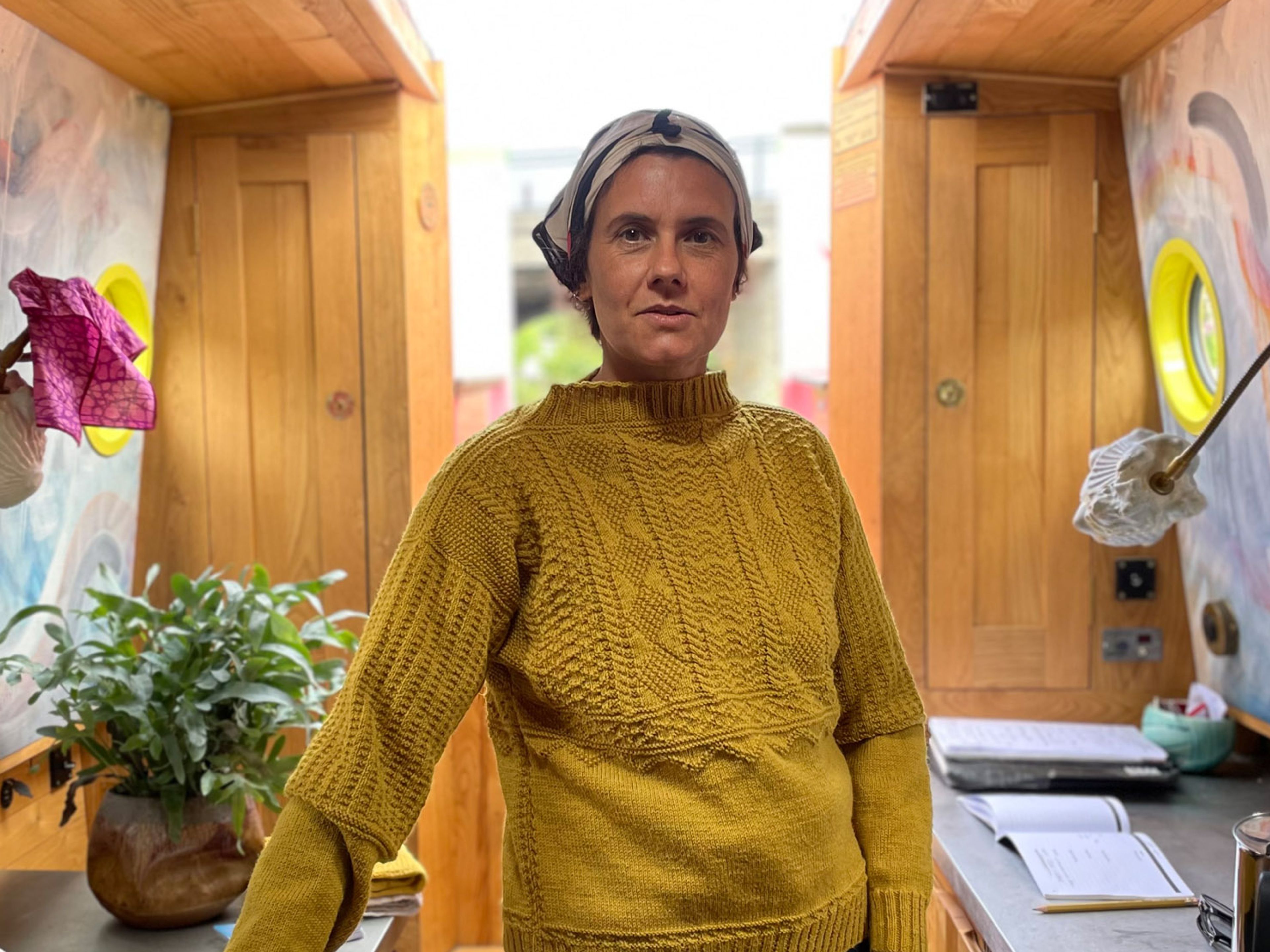 Heather is wearing a yellow jumper and headscarf. She is stood in a canal boat.