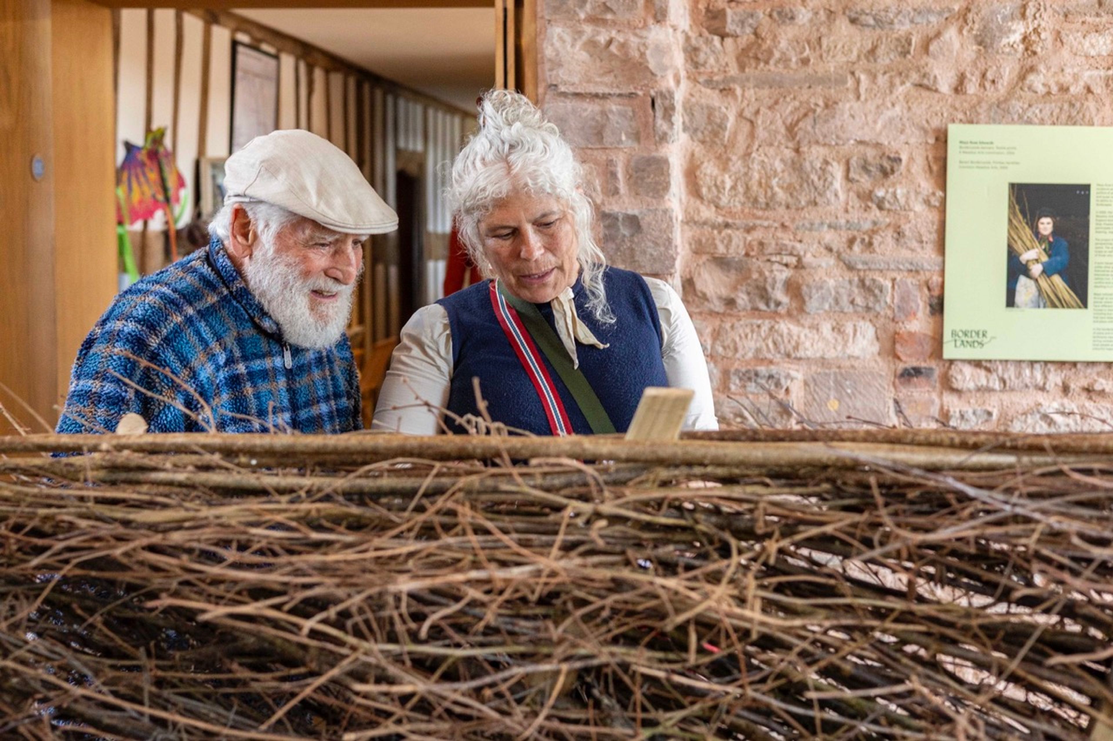 Two visitors view Maya Rose Edwards’ hazel stick hedge artwork 'Out of Bounds', in the BorderLands exhibition at Hay Castle. 