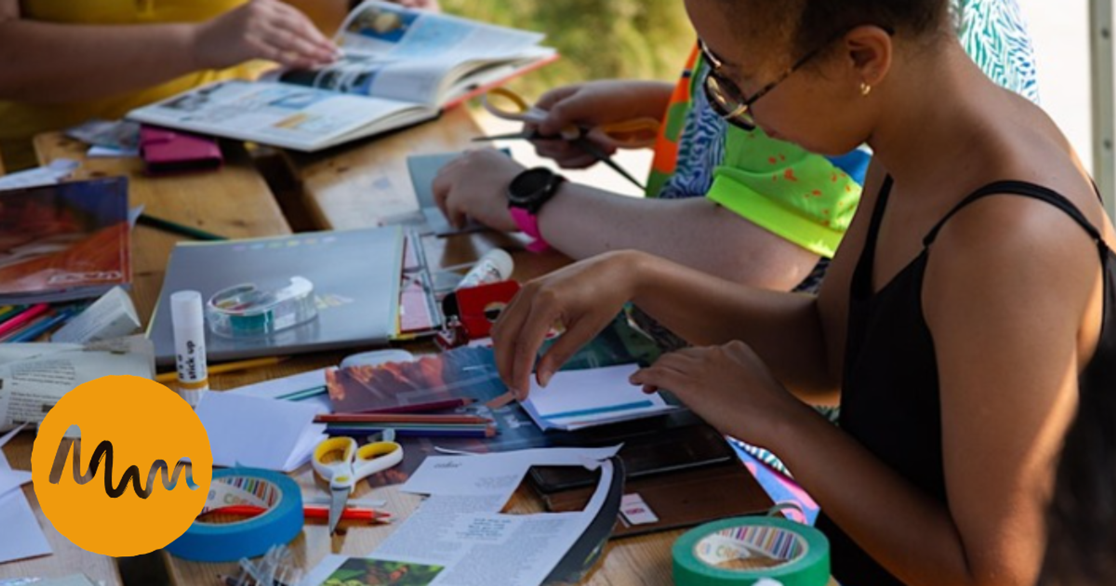 People making collages at a shared table using paper, scissors, glue and magazines during a creative workshop.