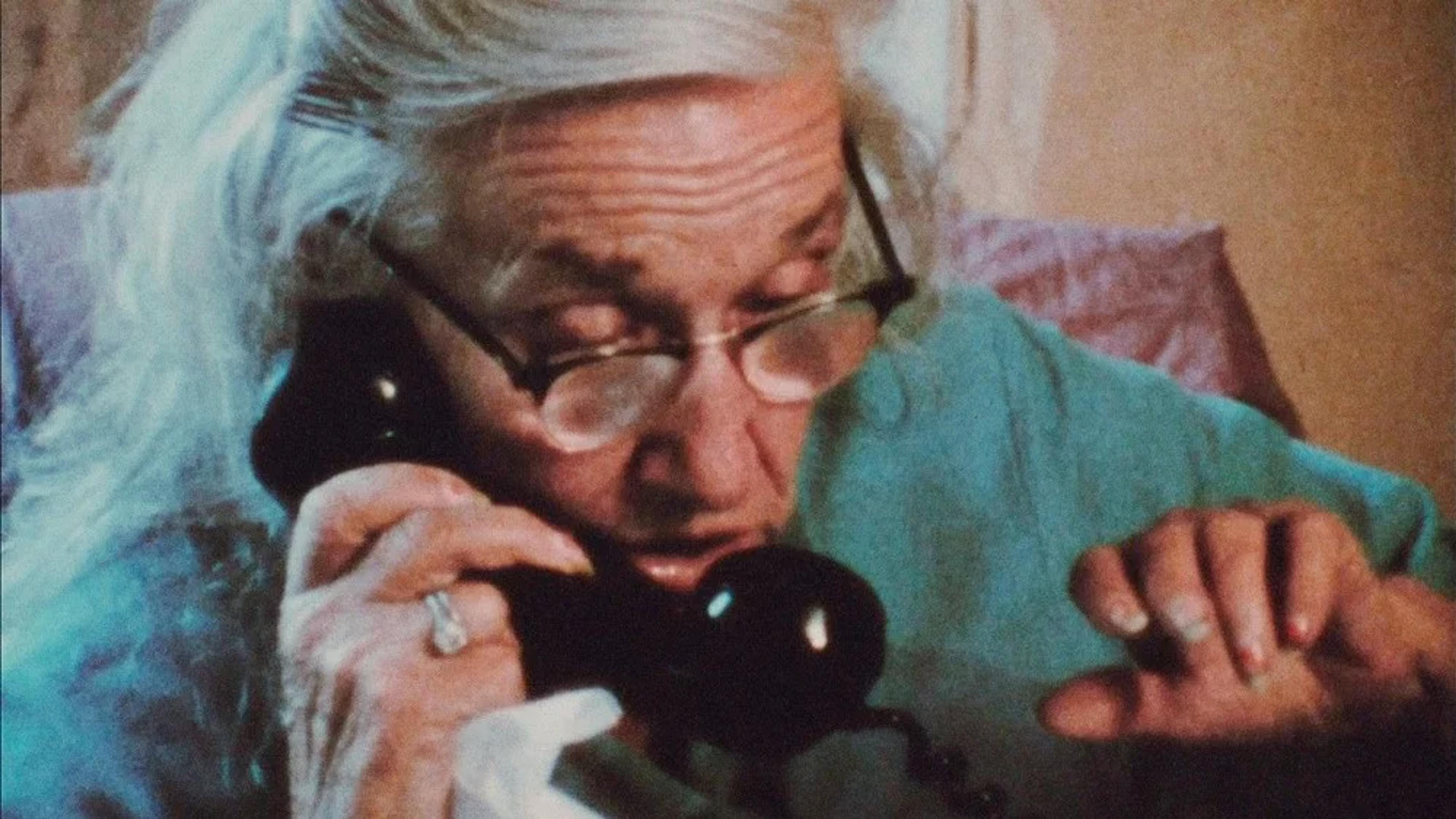 A photograph of an elderly woman using an old fashioned telephone. 