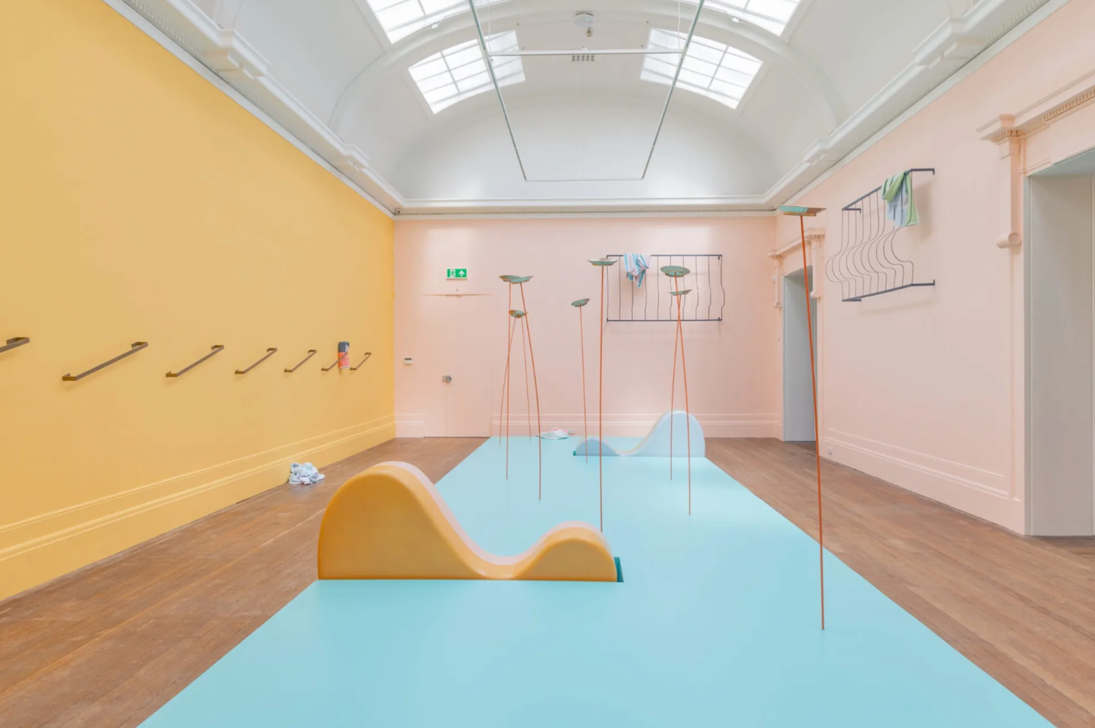 An installation of motionless spinning plates on a pale green floor, with pink and orange walls.