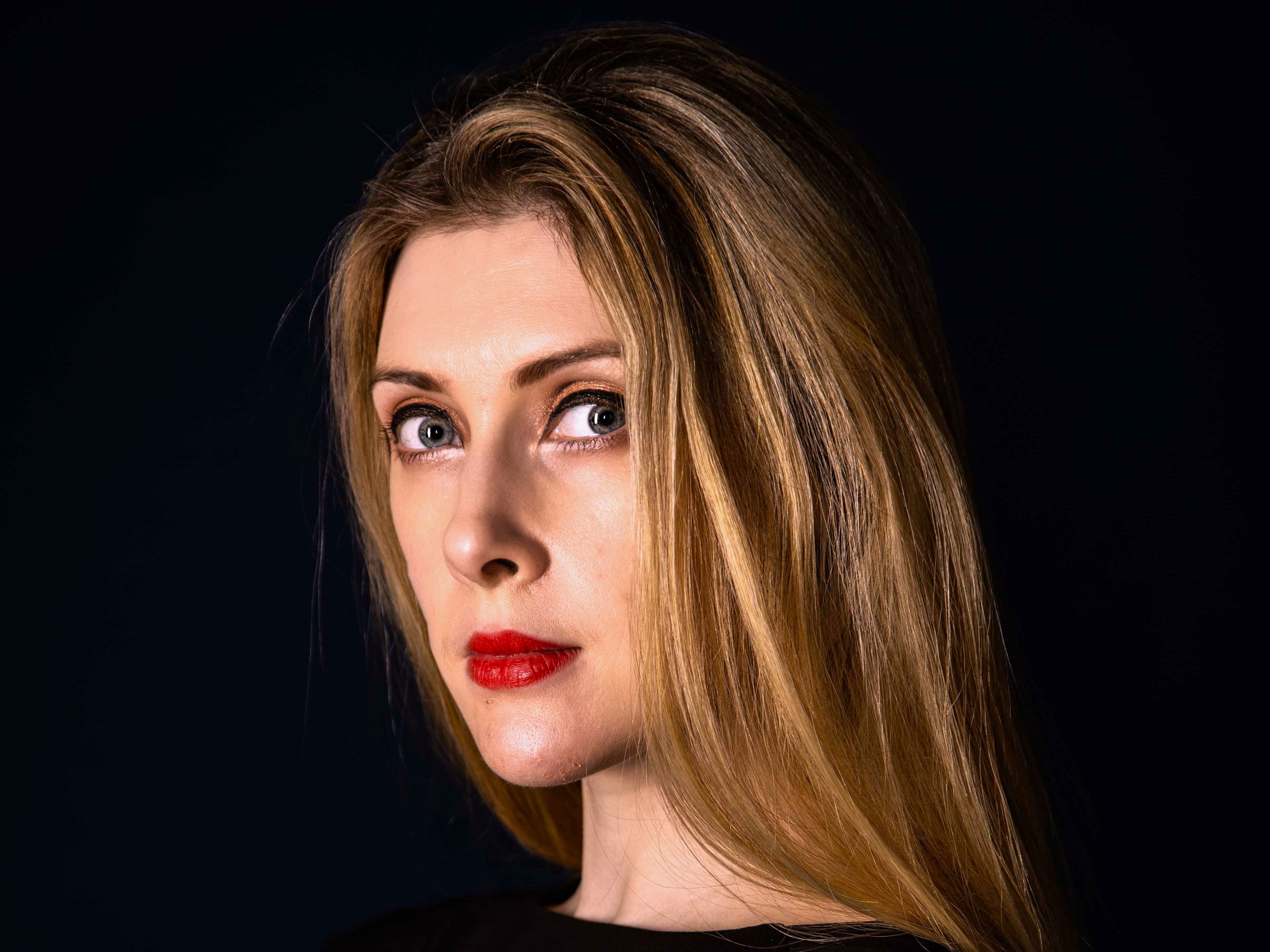 A side profile of Hannah Taylor in a black jumper with a black background.