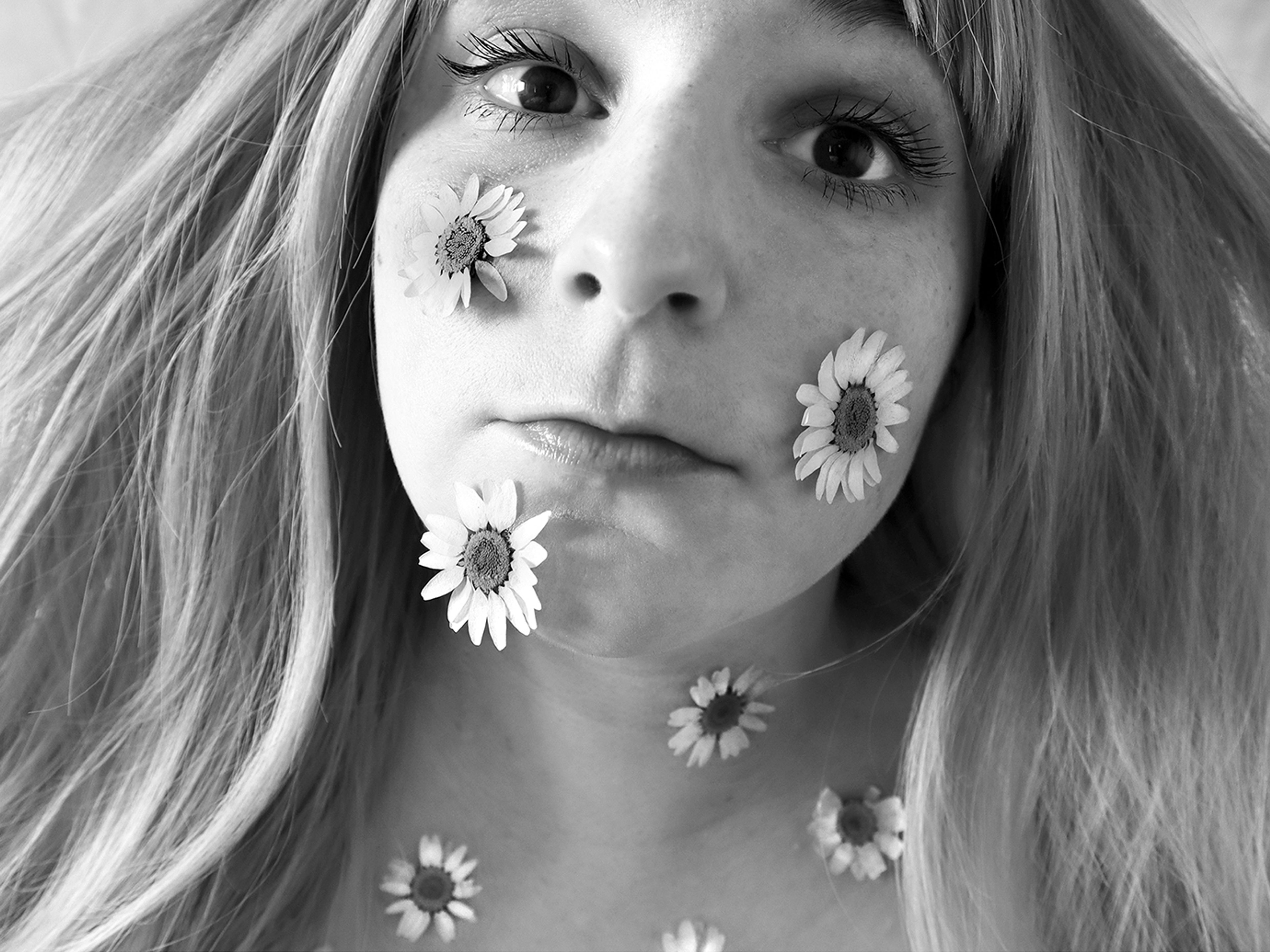 A black and white self portrait of the artist with daisies placed on their face and neck.