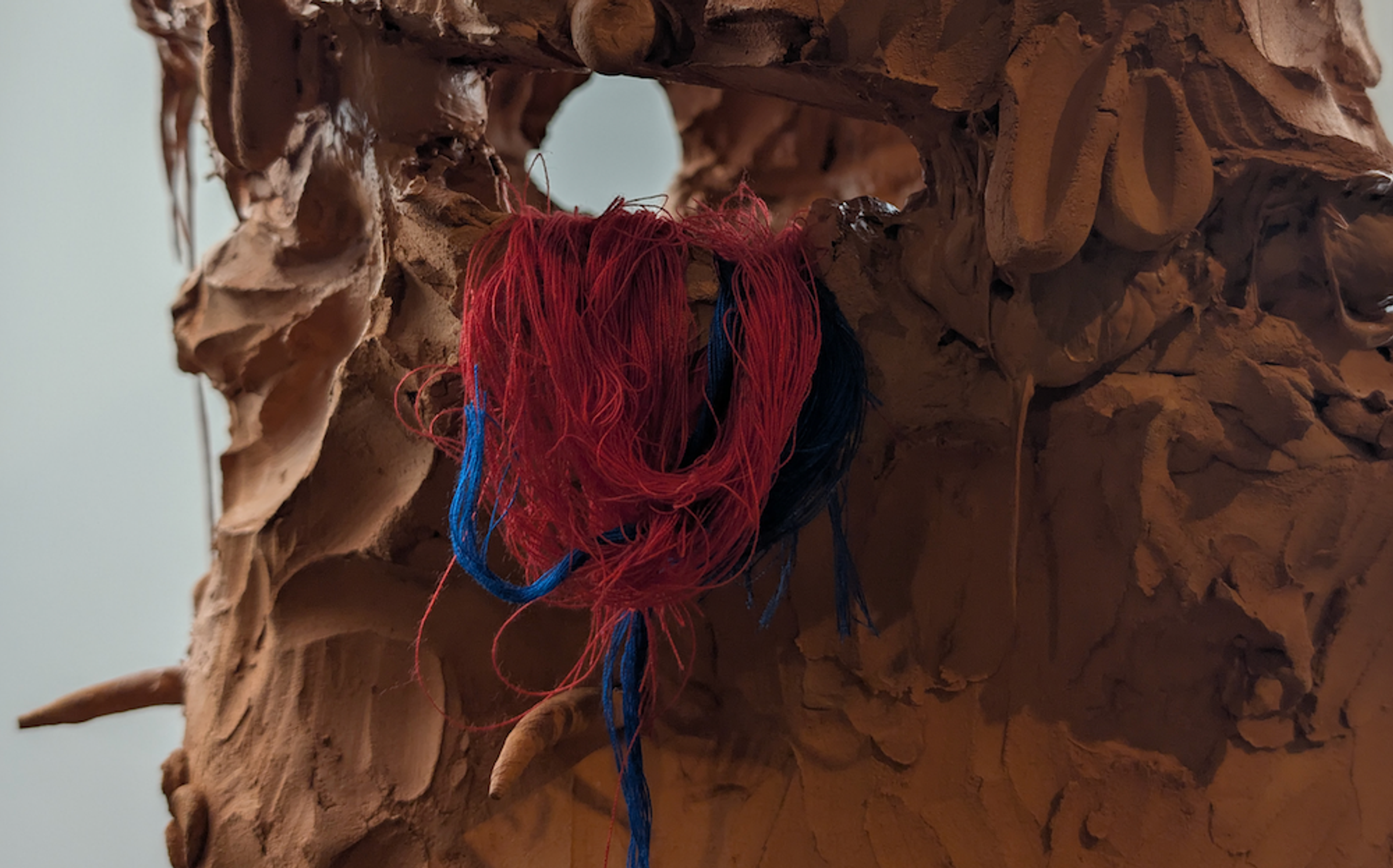 A close-up image of Abraham Babajide Cole's clay sculpture. Red and blue thread is looped through a hole in the clay.