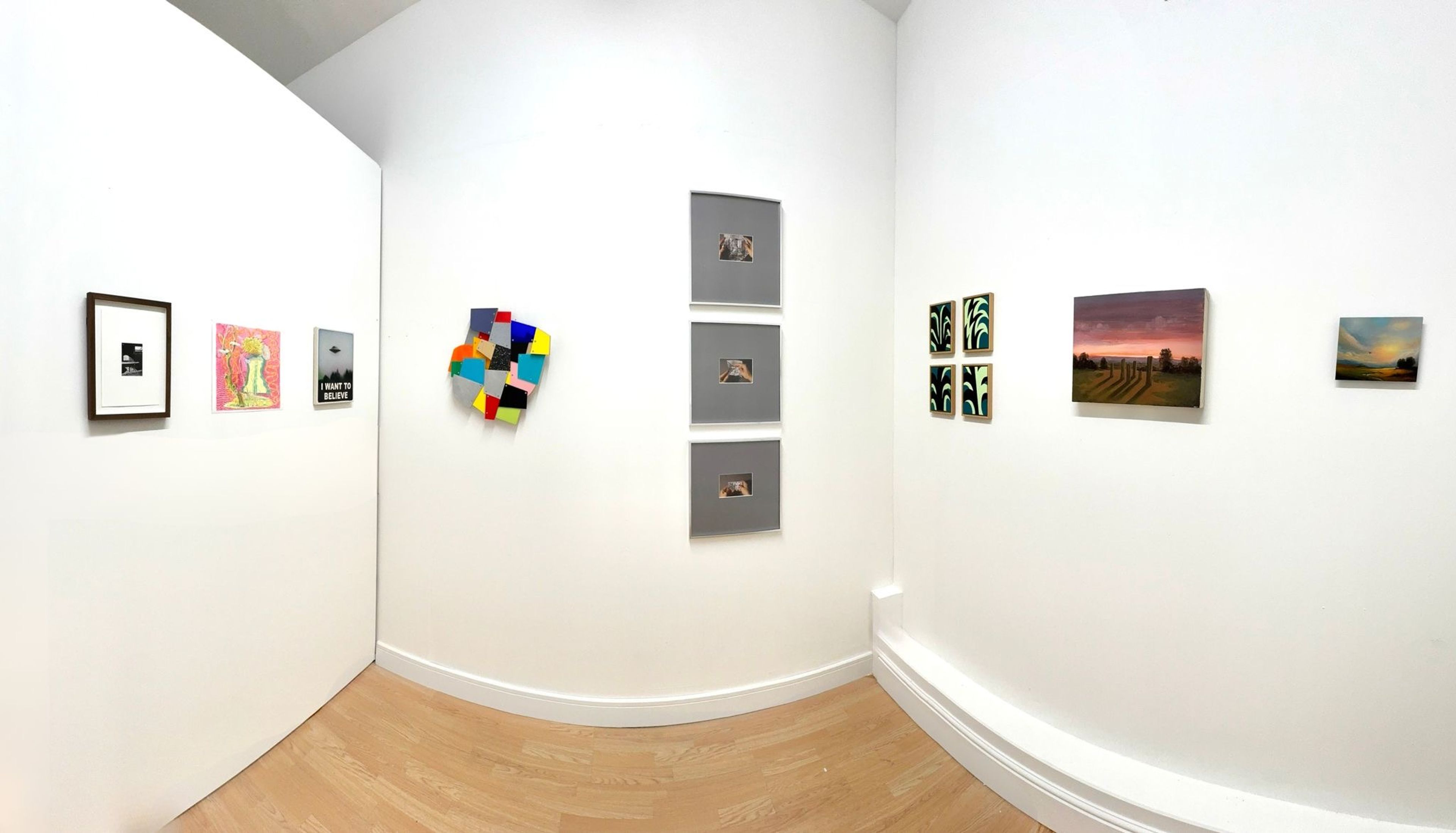 A fish-eye style photograph of the gallery with art works, white walls and a brown wooden floor.