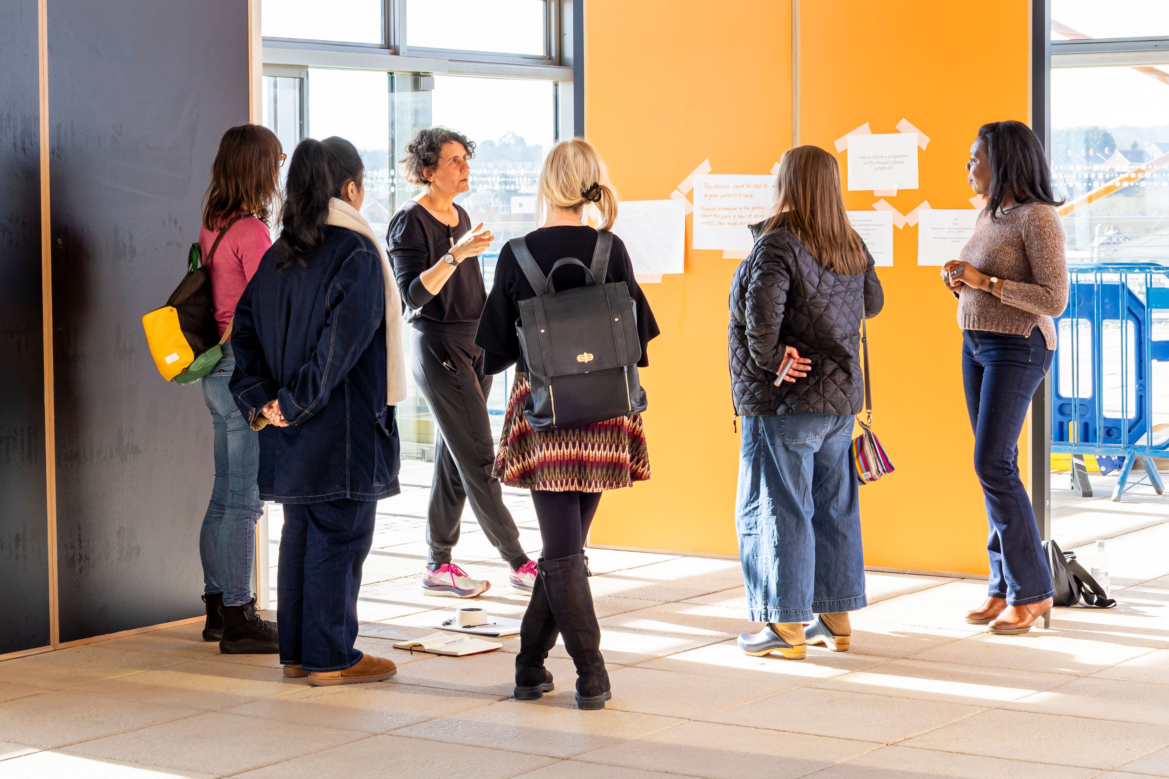A group of people stood in front of black and orange gallery walls with large note paper on.