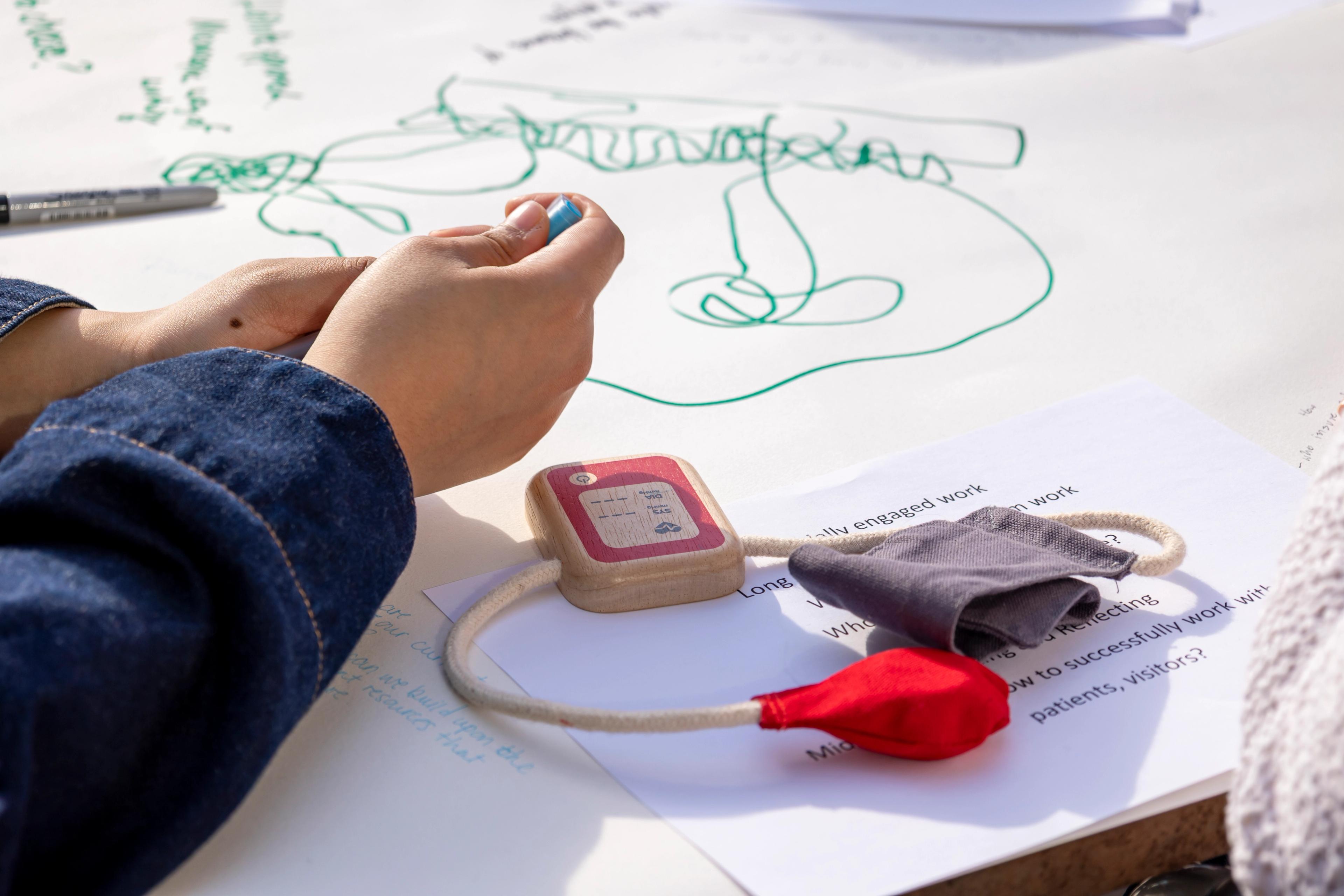 Hands with a pen over a large sheet of paper with lots of scribbles. A wooden toy stethoscope is on the right.