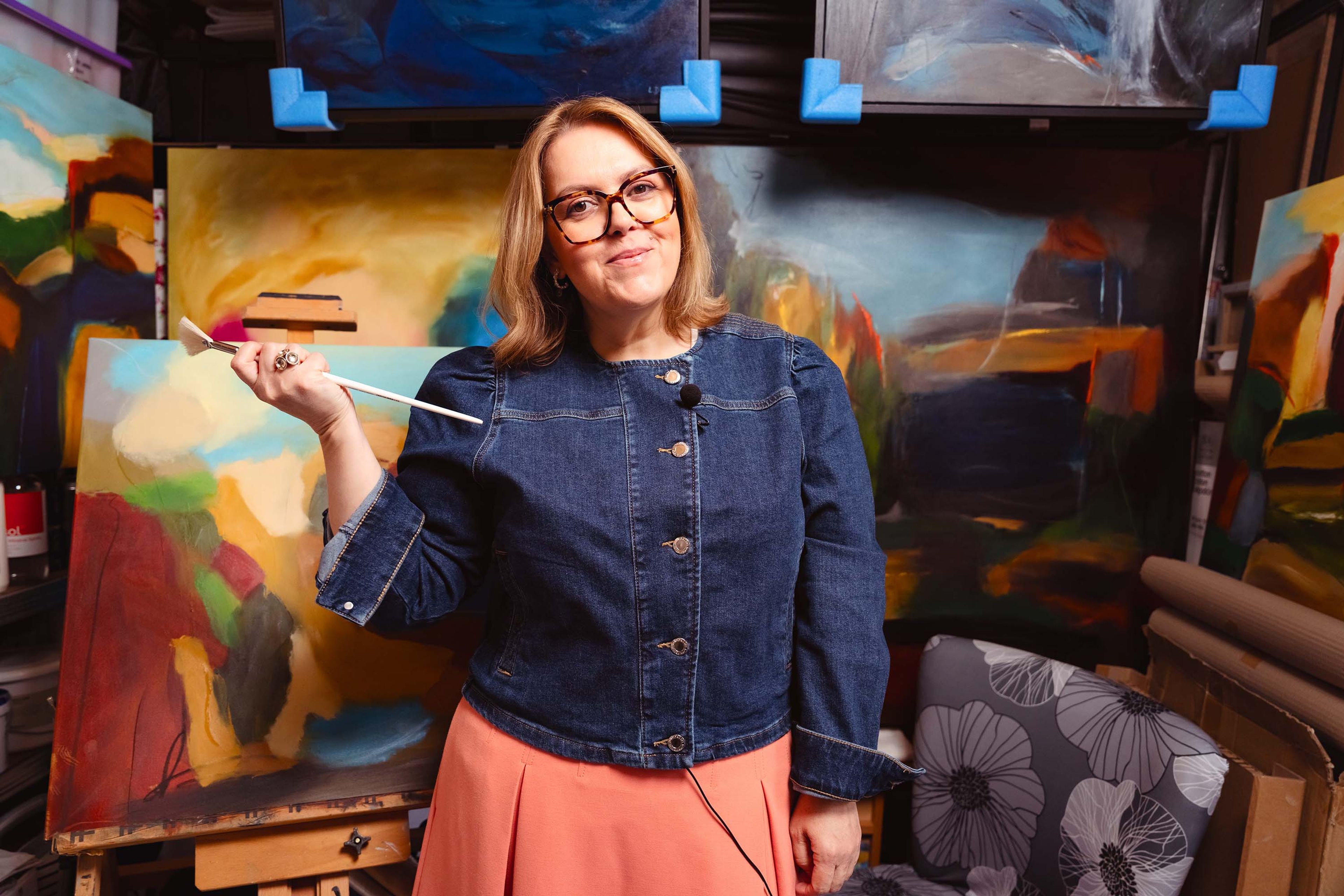 Image of Liliana Dobbs, (participating artist) holding a brush in front of her artworks