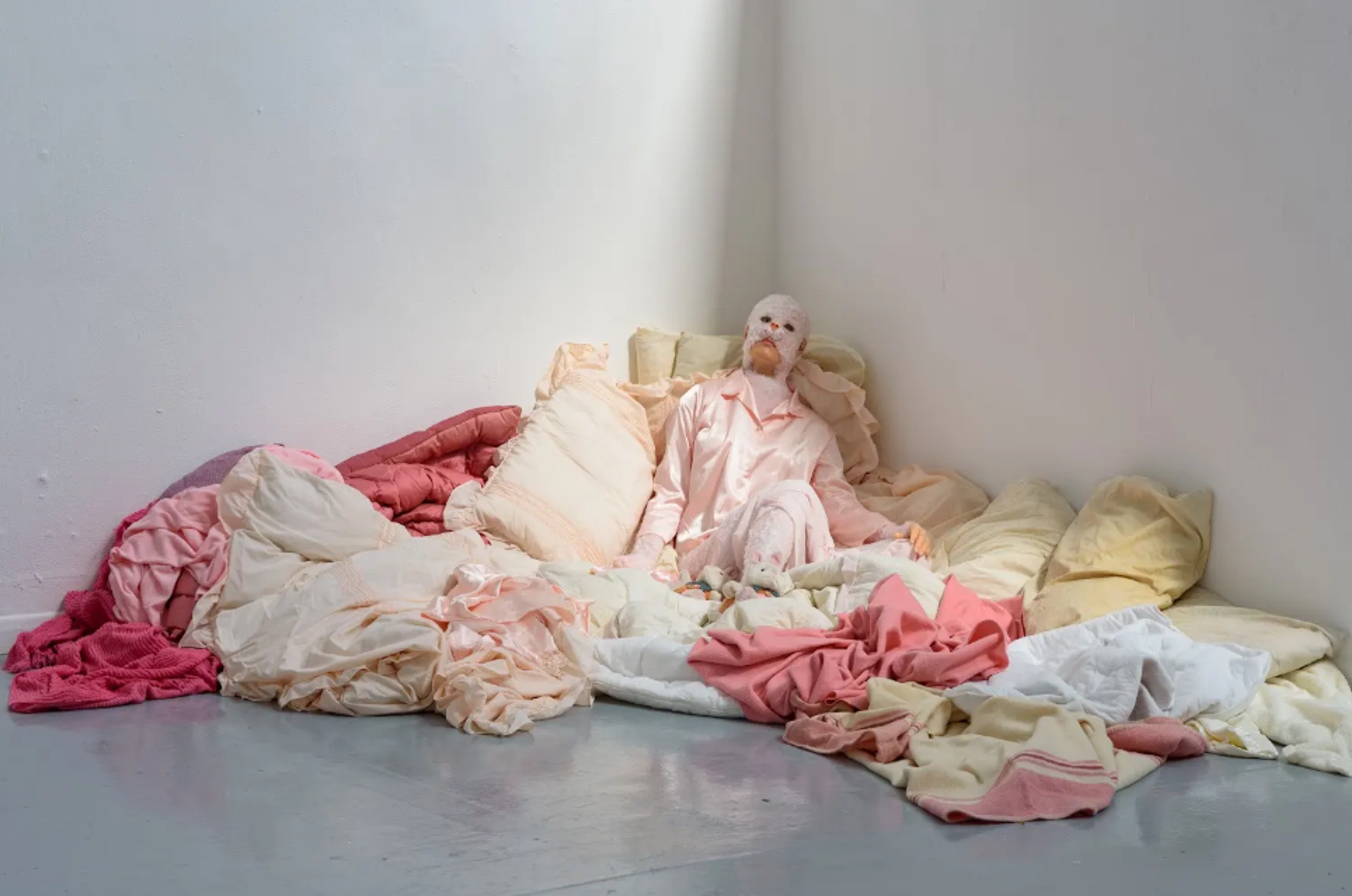  figure wearing a cat mask lying amongst lots of fabric