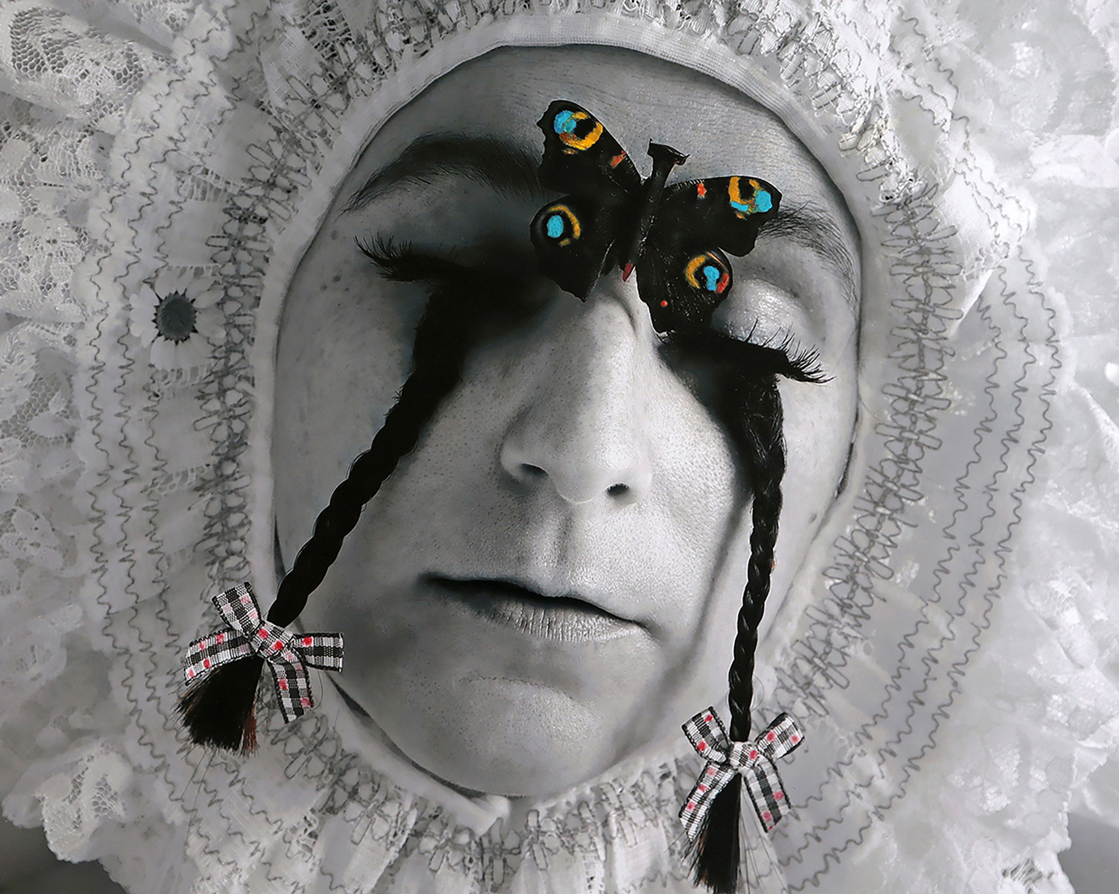 A face in black and white with closed eye and small braid emerging from the lower eyelid. A butterfly is on their forehead.