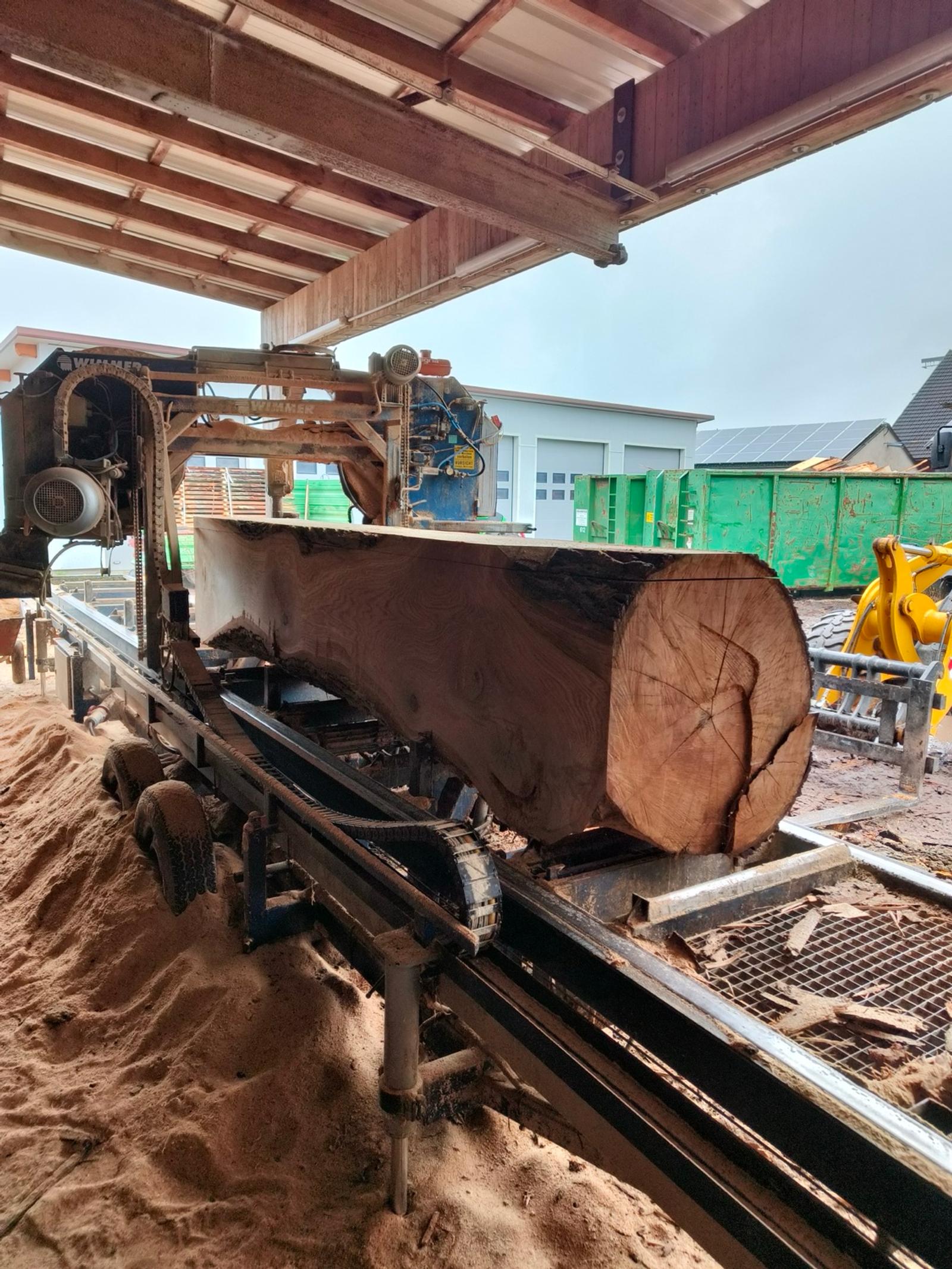 Massiver Baumstamm auf Schneidebahn, dunkles Holz, sichtbare Rinde