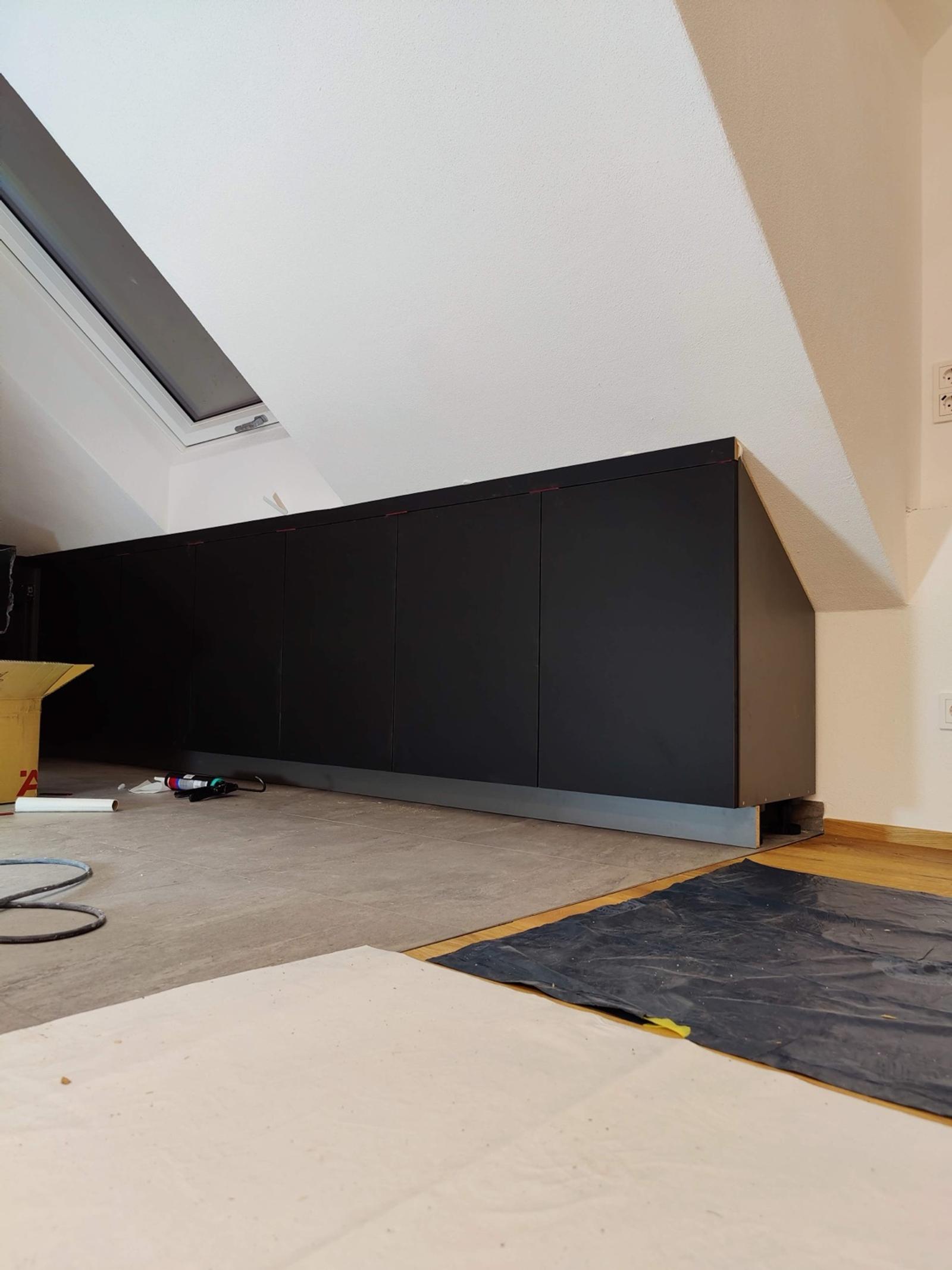 Schwarze Schränke aus Spannplatten unter Dachschräge mit Fenster
