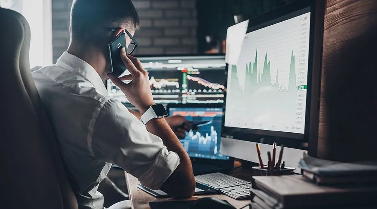 Sales tracking guide man holding a phone looking at charts on a computer