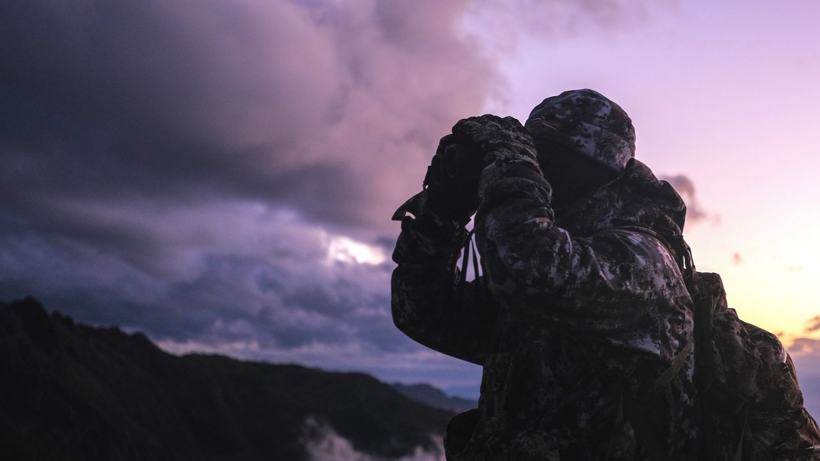 Hunter glassing the tops through binoculars at dusk