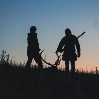 Two hunters silhouetted against a dusk sky, dragging a stag by its antlers through long grass, one with a rifle slung over his shoulder, with the word "Tipping" in bold distressed lettering across the top.