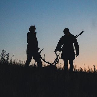 Two hunters silhouetted against a dusk sky, dragging a stag by its antlers through long grass, one with a rifle slung over his shoulder, with the word "Tipping" in bold distressed lettering across the top.