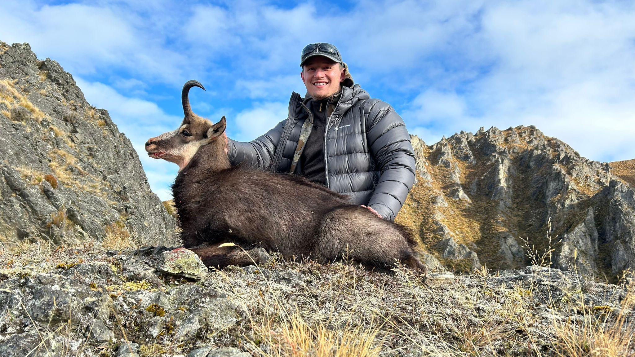 A hunter in a puffer jacket with a chamois on a rocky ridge
