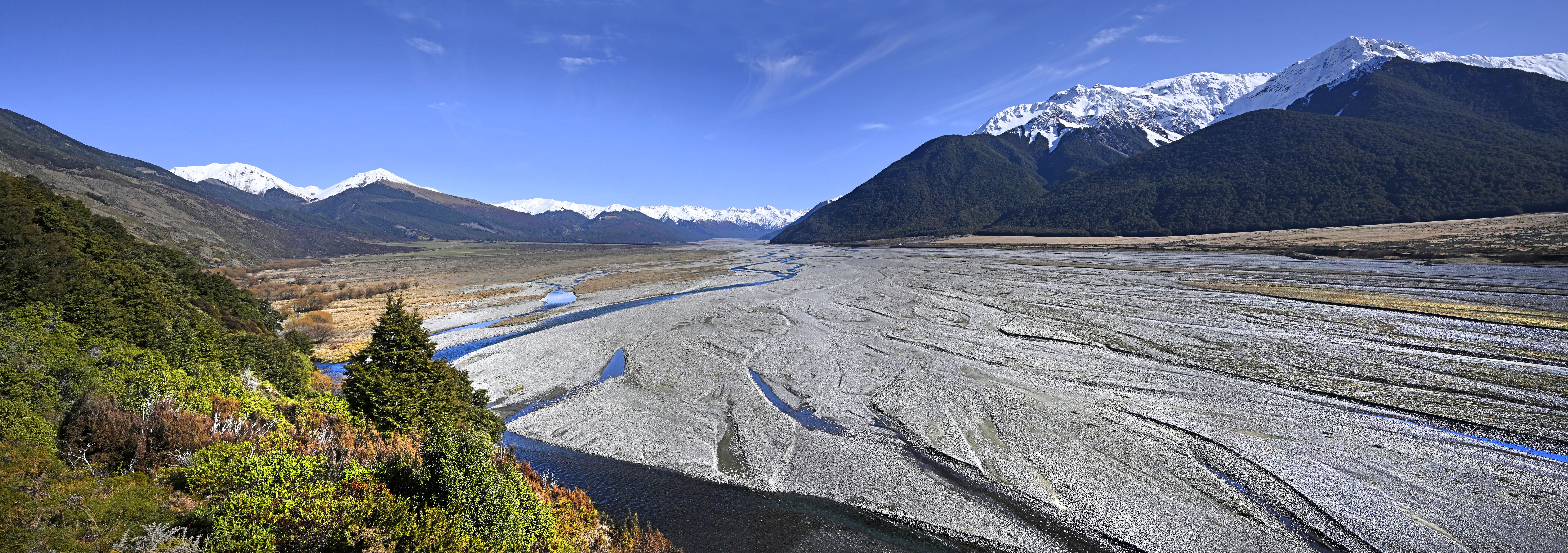 Braided river spreading across a wide shingle bed below snowy ranges