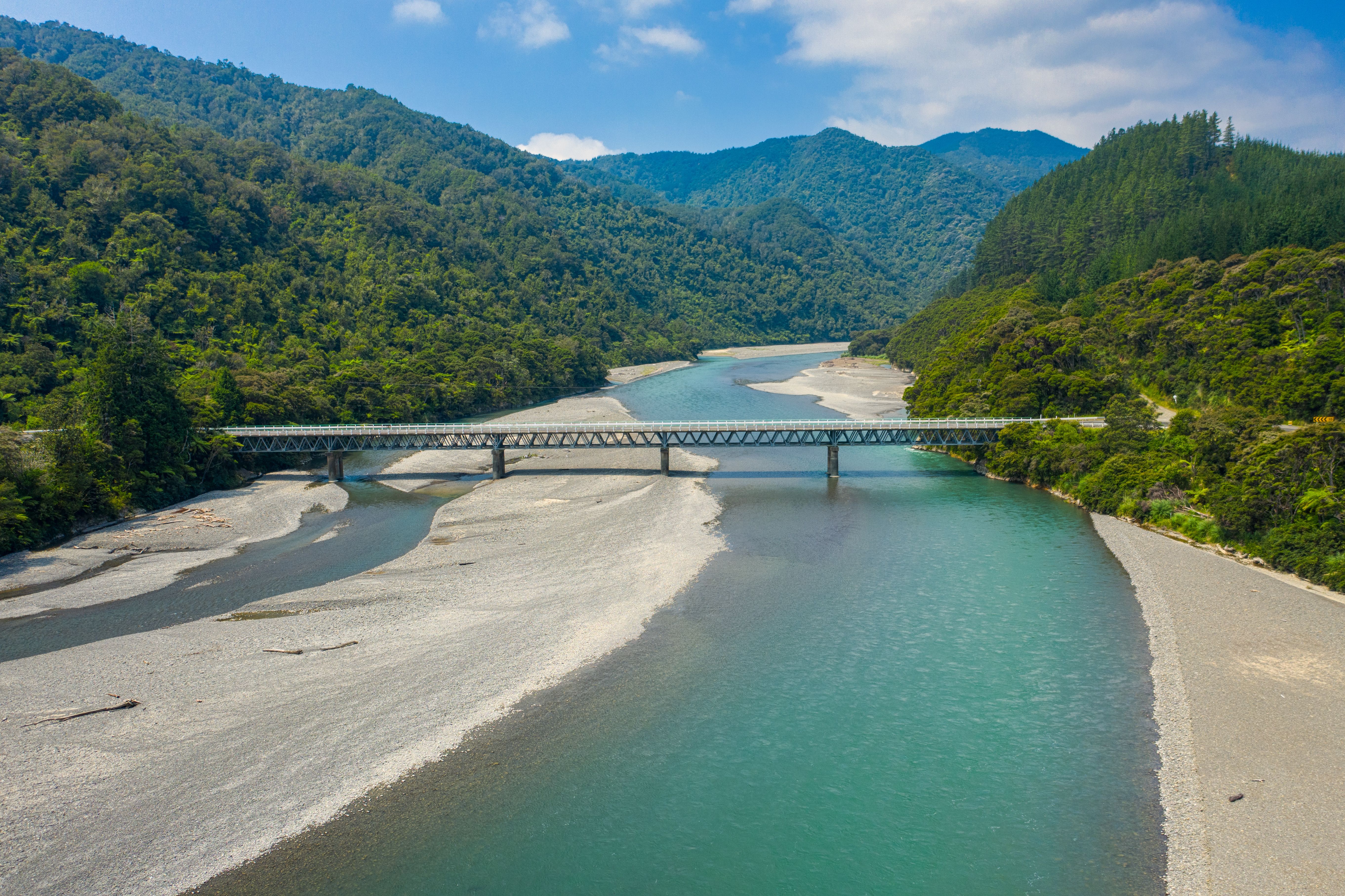 Road bridge crossing a milky green river between bush-clad hills