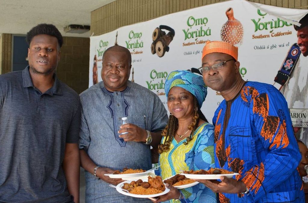 Four members hold plates of jollof rice in front of the Omo Yorùbá banner