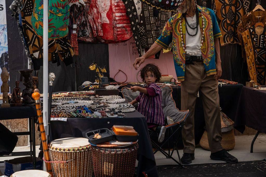 A toddler sits at a jewelry stall while the vendor reaches over the beads
