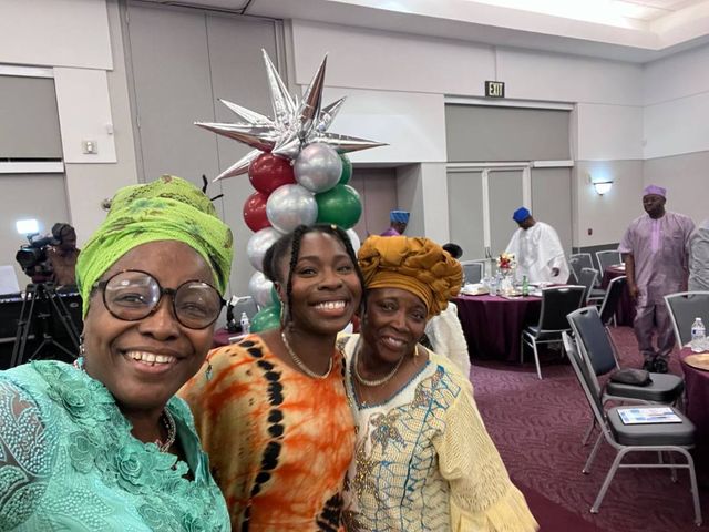 Three women take a selfie in front of the red, silver and green balloon arch