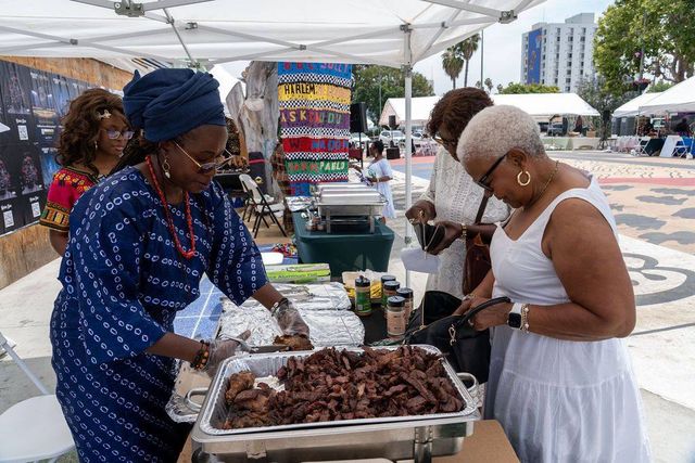 A vendor in indigo àdìrẹ serves suya to a guest in white
