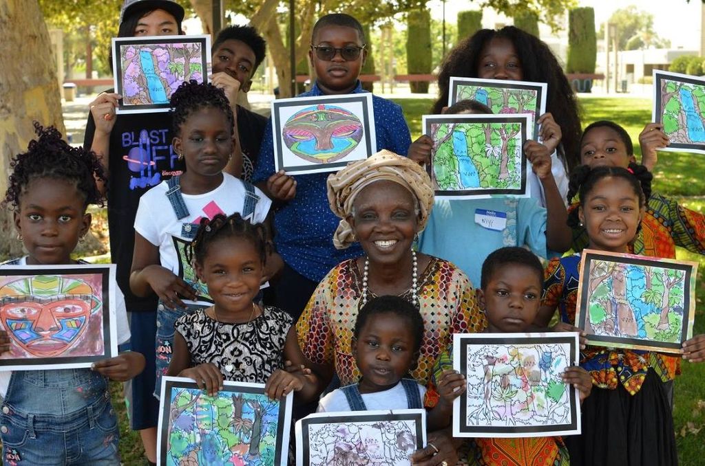 The children and their teacher show their drawings outdoors
