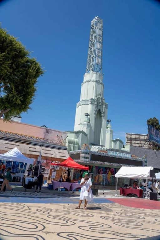 A woman in white speaks into a microphone on the plaza below the Vision Theatre tower