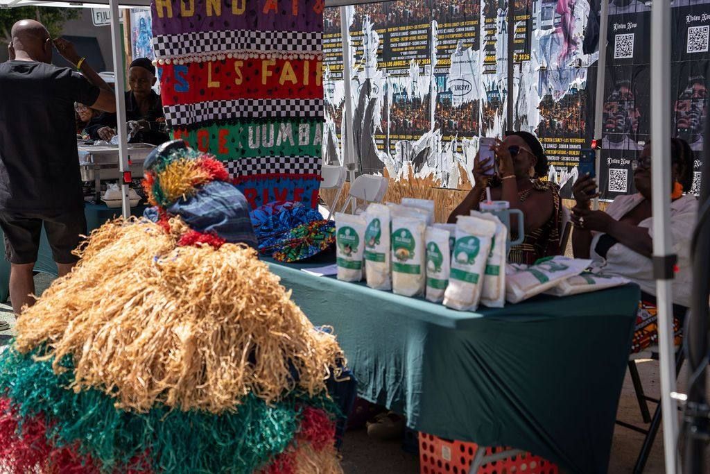 The raffia masquerade rests beside a food stall