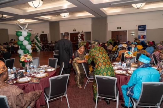 Guests greet each other between the round tables in the hall, green and white balloon columns behind