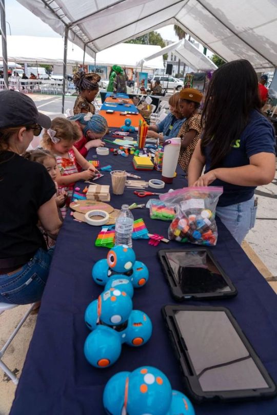 Children build with craft sticks at a long table lined with small blue robots