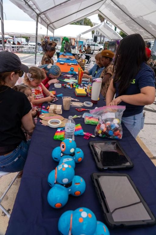 Children build with craft sticks at a long table lined with small blue robots