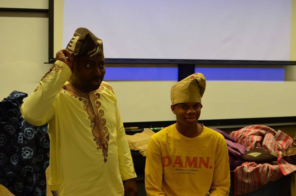 A man in embroidered agbada adjusts his fila while a teenager tries on his own
