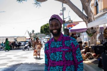 A man in a purple and teal print shirt and cap smiles on Degnan Boulevard