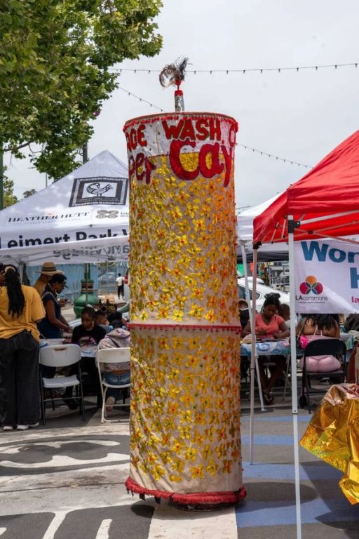 A tall cylindrical masquerade covered in yellow flowers stands between the tents
