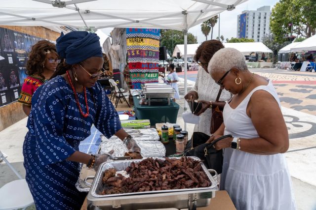 A vendor in indigo àdìrẹ serves suya to a guest in white