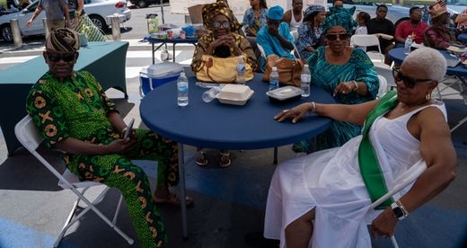 Elders in aṣọ òkè and lace rest at a round table in Ọjà Balógun, the market