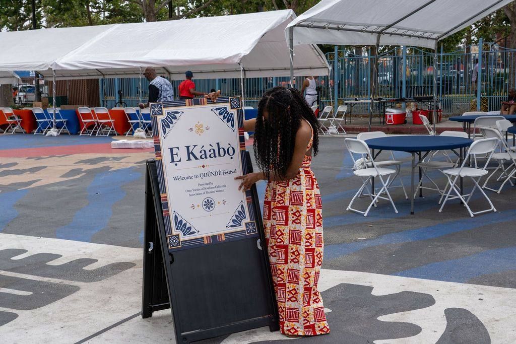 A volunteer sets the Ẹ Káàbọ̀ welcome sign on the plaza