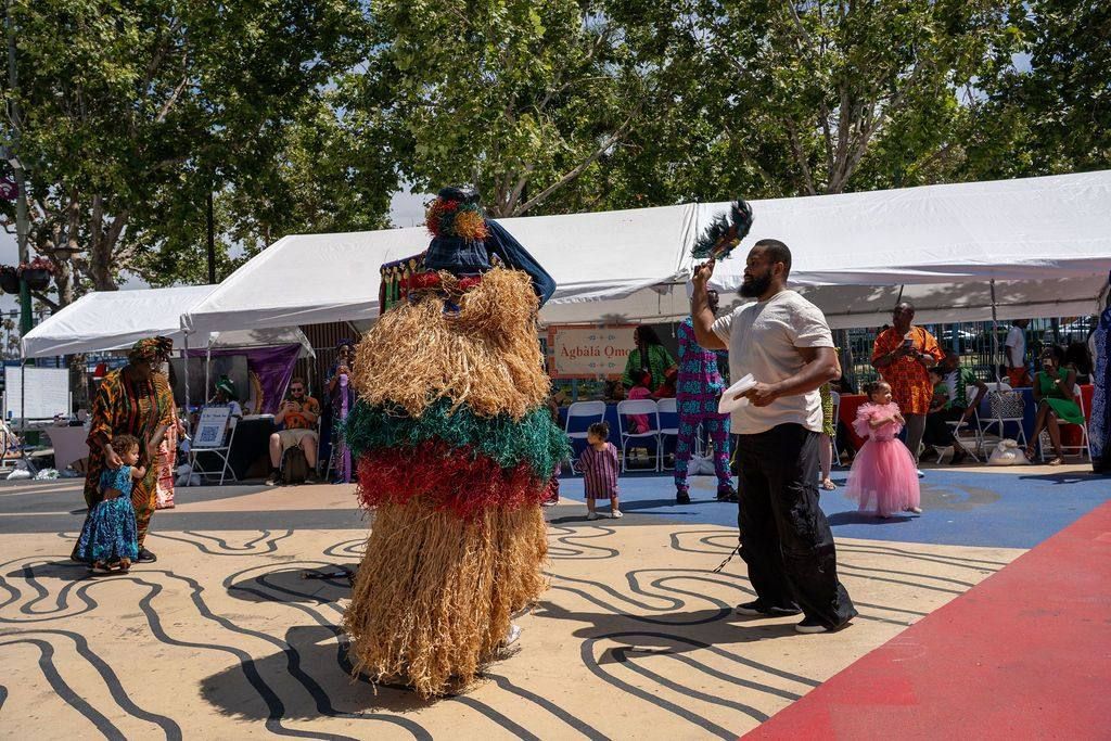 A raffia masquerade dances in front of the Àgbàlá Ọmọde tent while a man fans it