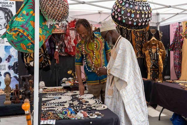 A vendor shows cowrie necklaces to an elder in white agbada