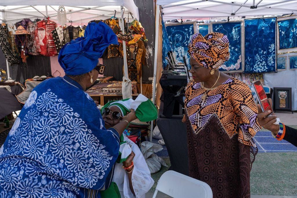 A woman in blue àdìrẹ ties a green and white gèlè on a seated guest