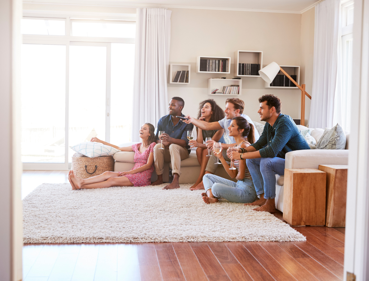 a group of people watching TV holding wine glasses in a bright room 