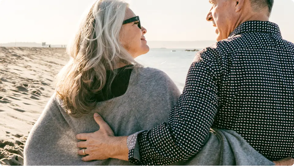 Middle-aged man and woman on a beach, smiling.