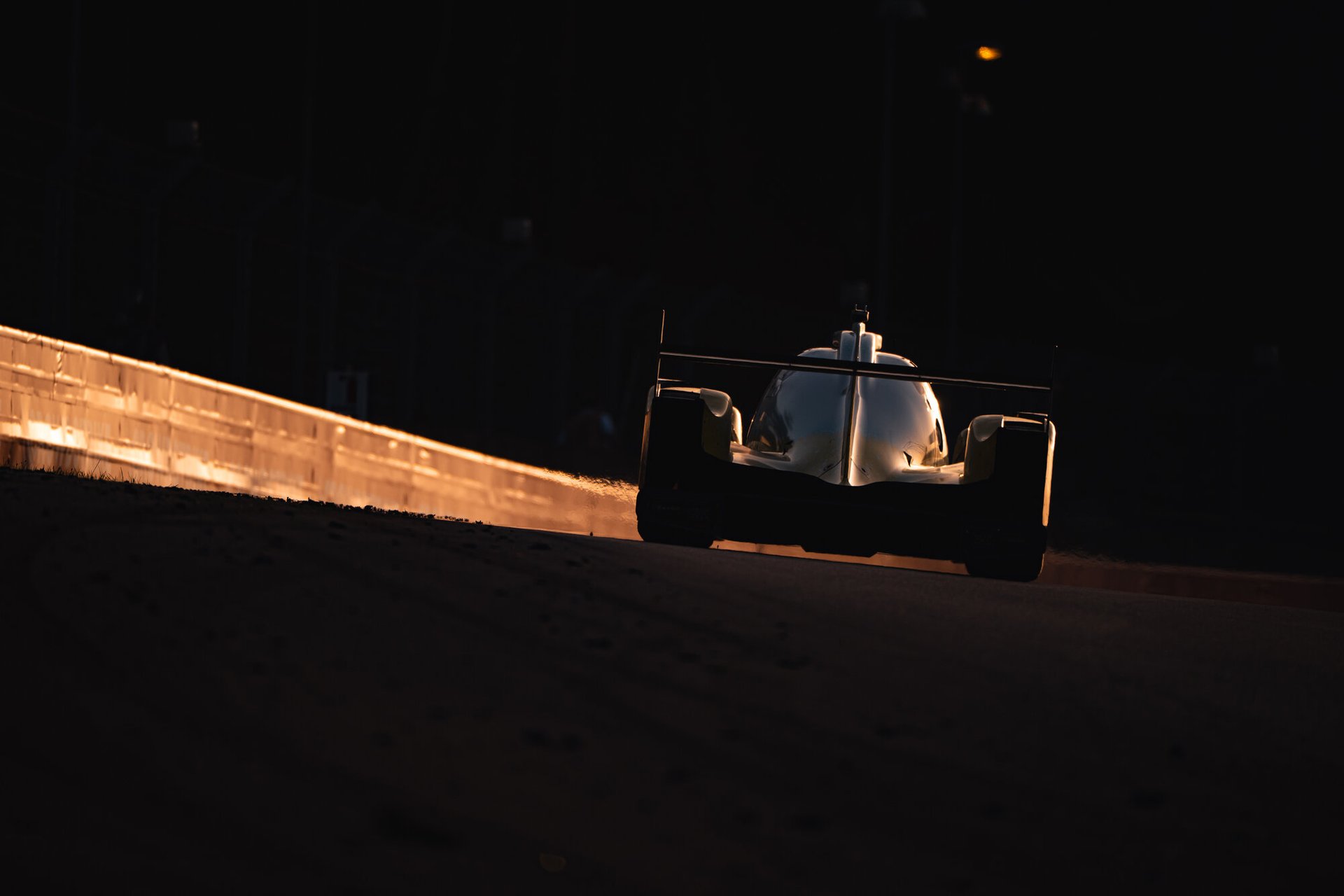 Inter Europol Oreca LMP2 silhouetted against the glowing barriers at dusk at Le Mans, backlit and almost black